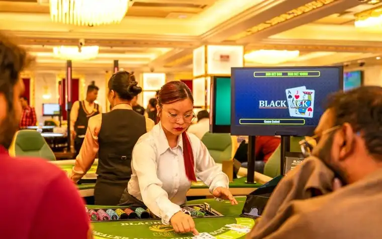 Dealer standing at a blackjack table while seated players watch the cards being dealt