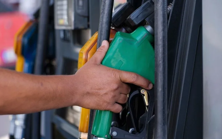 Close-up of a hand holding a green fuel nozzle at a gas station pump