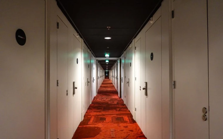 Long hotel corridor with red patterned carpet leading toward guest room doors