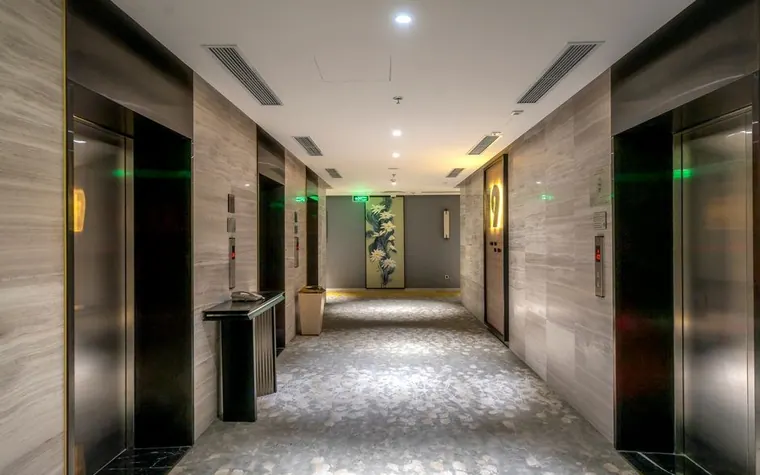 Hotel hallway with elevator doors and patterned stone floor tile leading to guest rooms